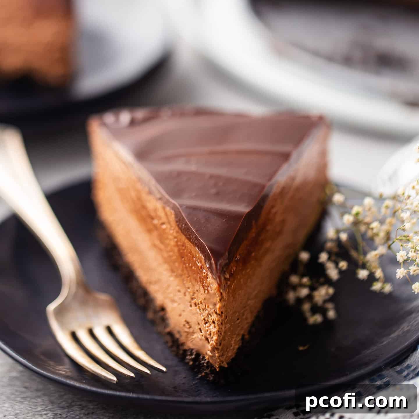 A perfectly portioned slice of no-bake chocolate cheesecake resting on a dark plate, accompanied by a vintage silver fork, ready to be enjoyed.
