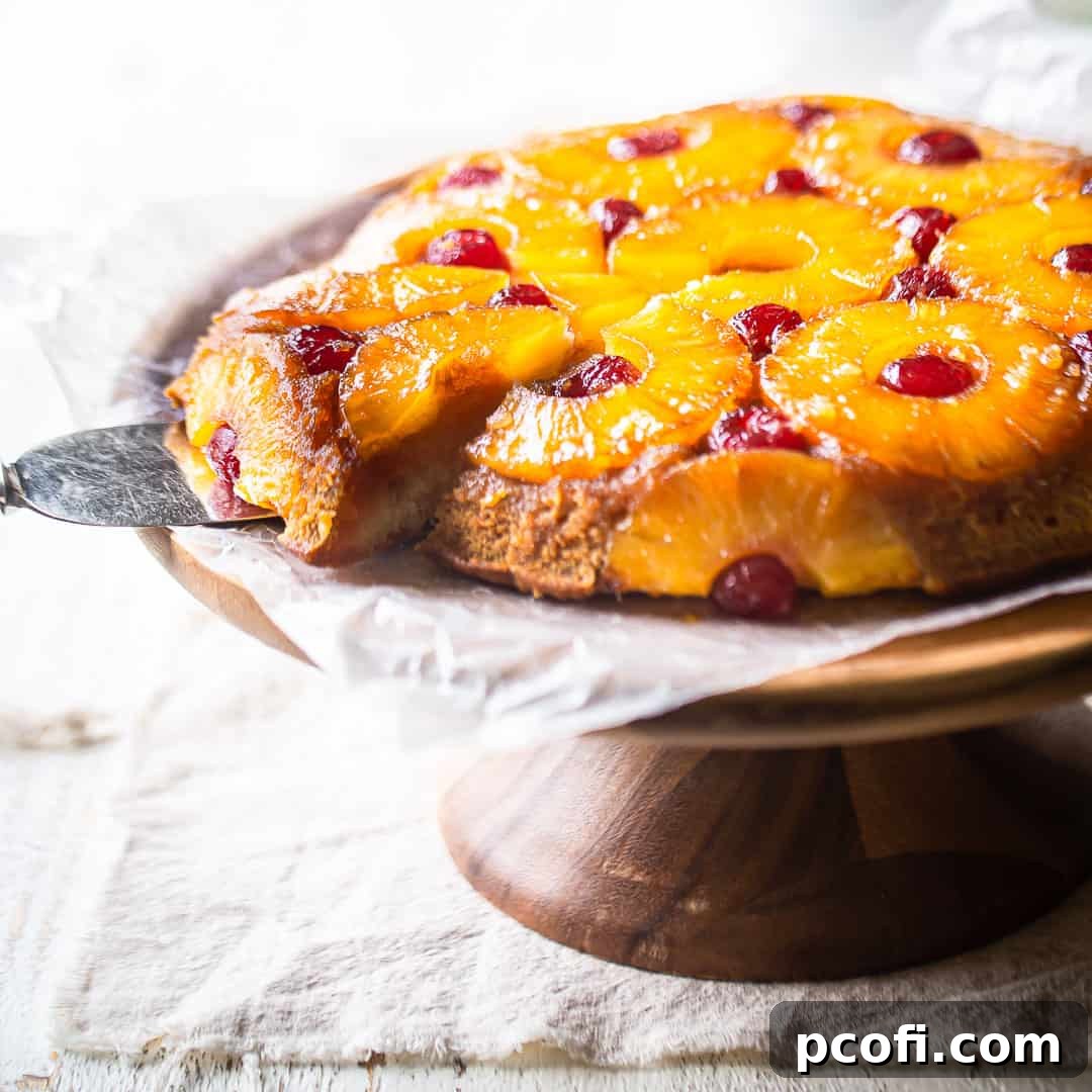Pineapple upside-down cake beautifully presented on a wooden pedestal with a vintage silver server, inviting a sweet taste.