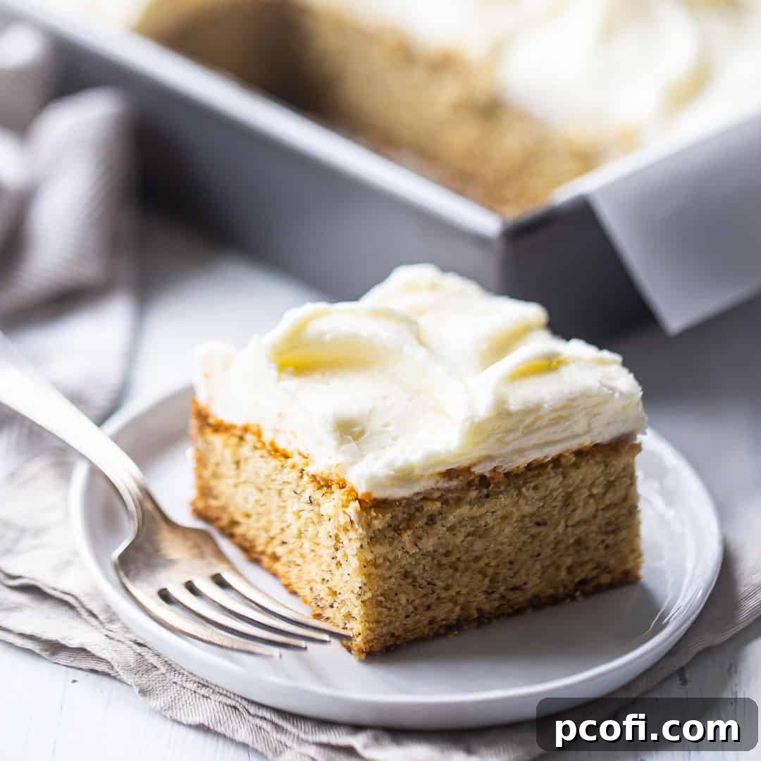 A square slice of moist banana cake, served on a white china plate with a silver fork, highlighting its inviting texture.