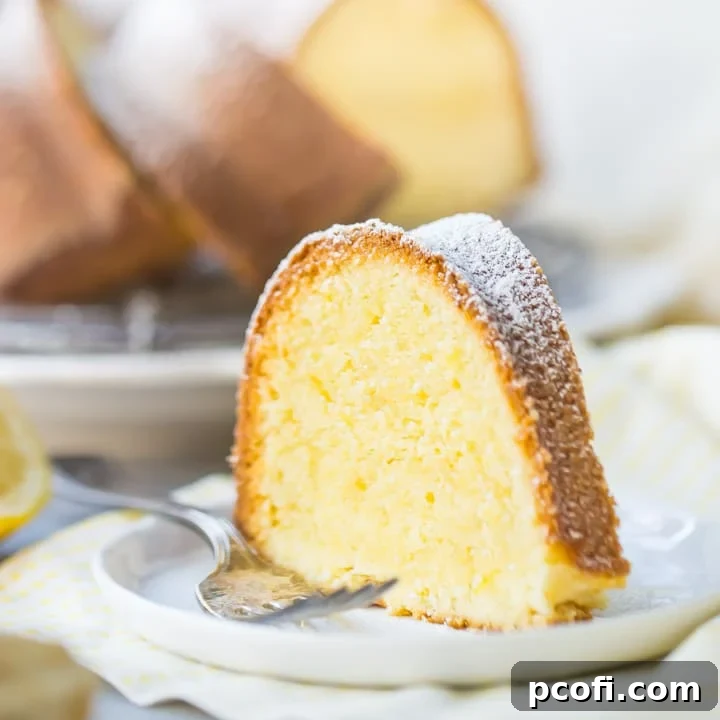 A tall, elegant slice of buttery lemon pound cake served on a white plate over a cheerful yellow napkin, accompanied by a gleaming silver fork.