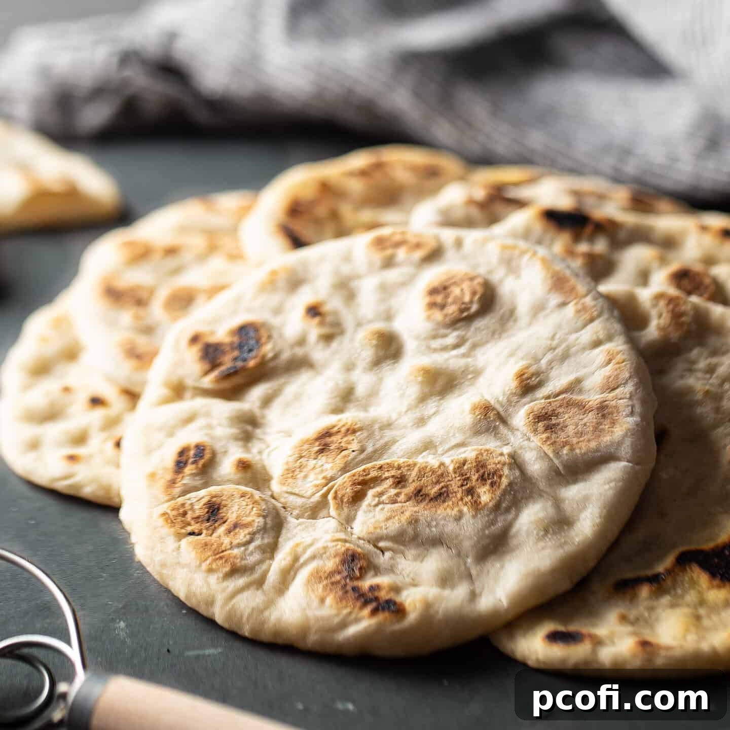 A stack of golden-brown pita breads, perfectly puffed and soft, arranged on a dark green background.