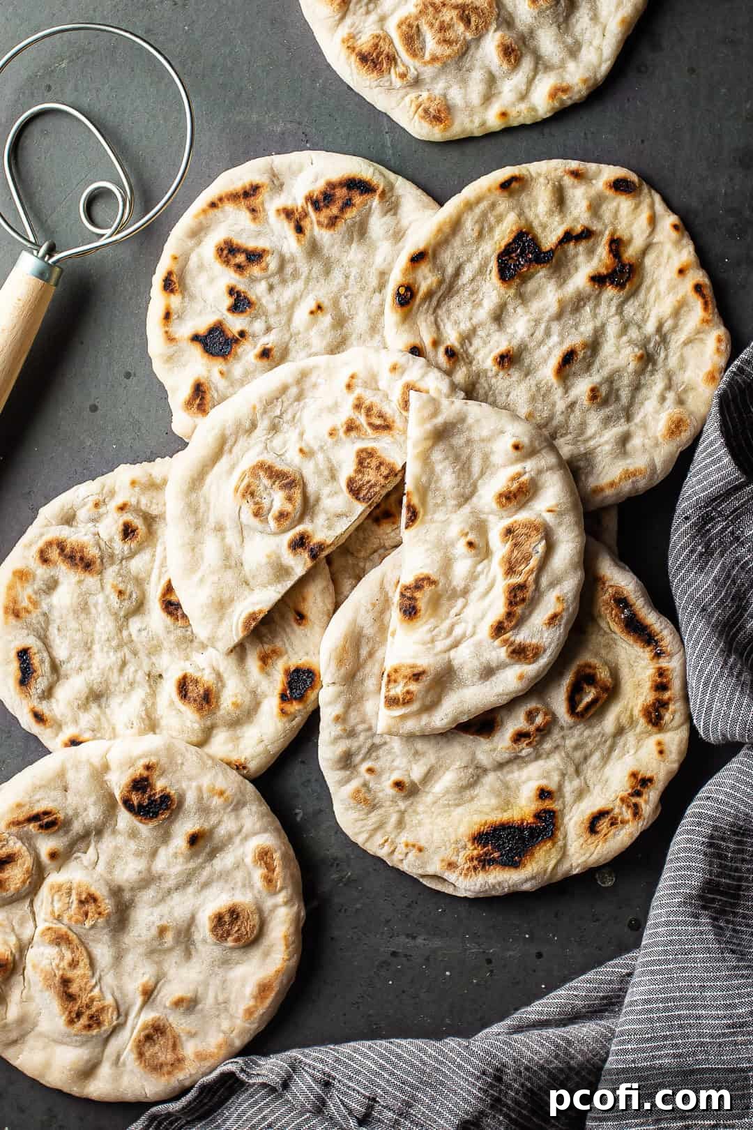 A beautifully presented stack of homemade pita bread, ready to be served, on a dark background with a striped cloth.
