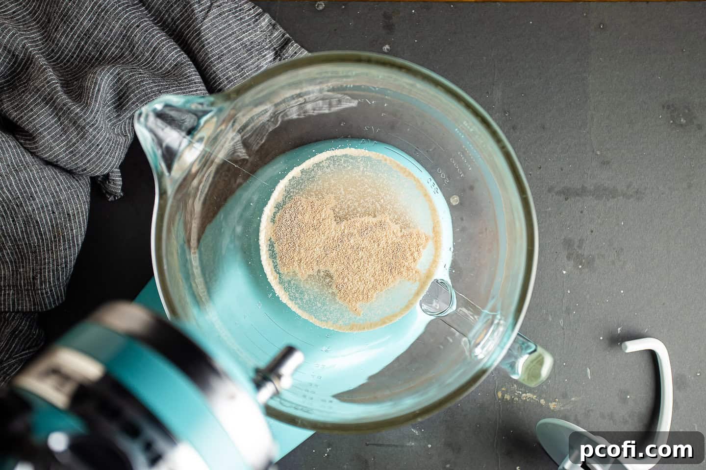 Active dry yeast dissolving and becoming foamy in warm sugar water in a glass bowl.
