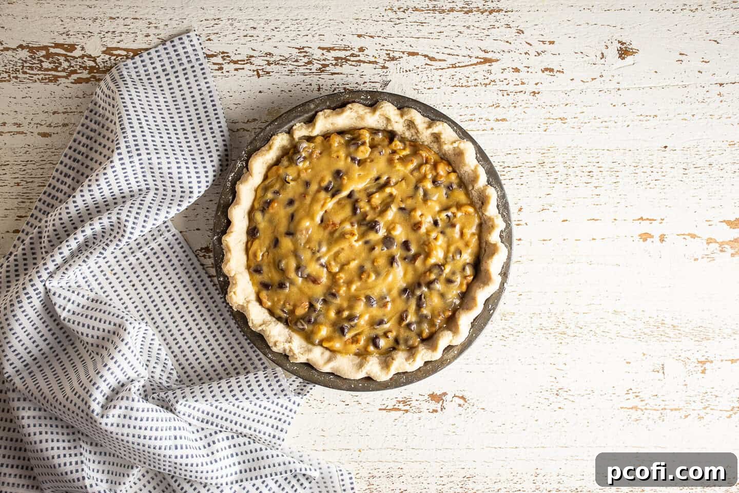 Unbaked derby pie in a vintage pie pan on a distressed white surface.