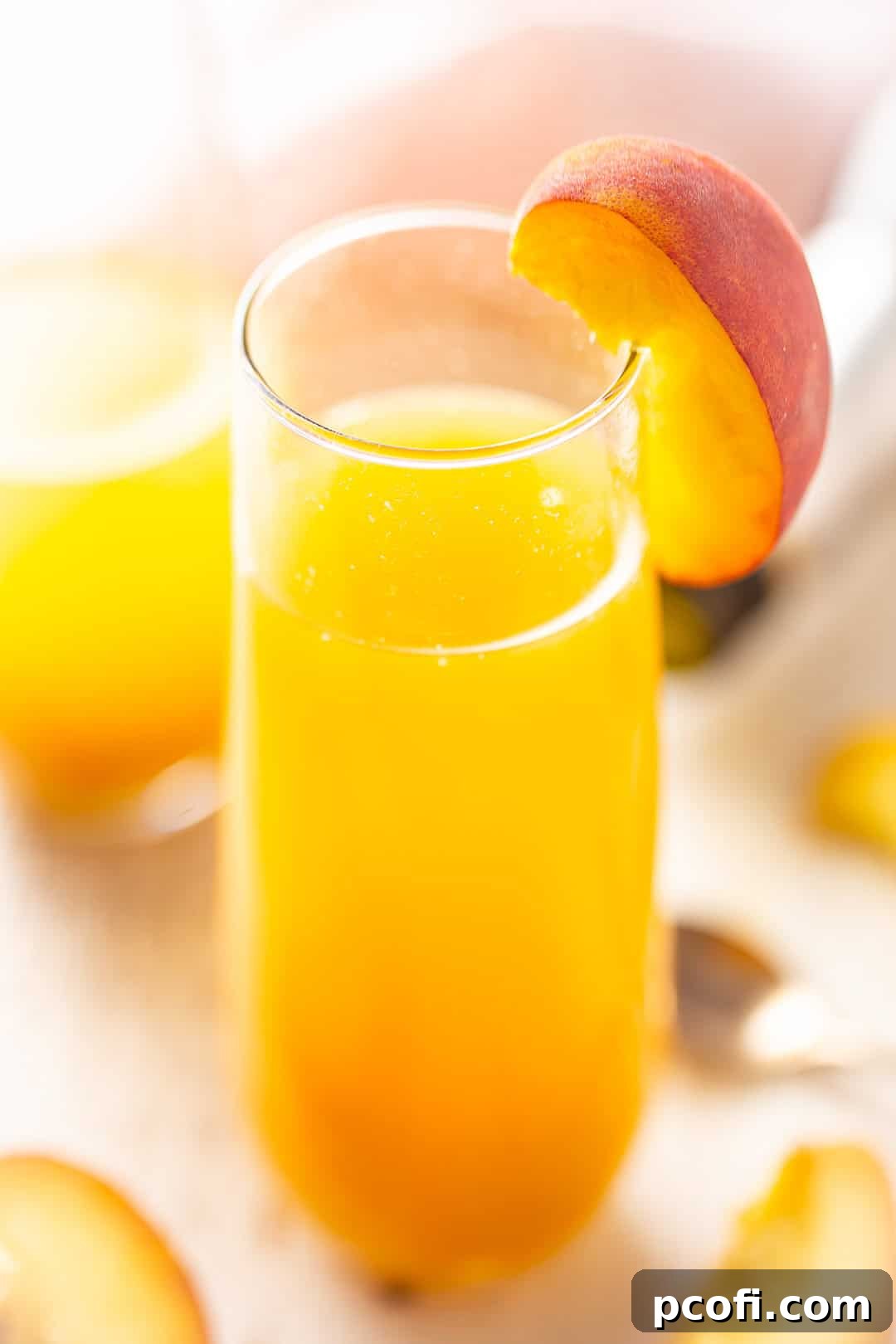 Two vibrant Peach Bellinis elegantly presented in stemless flutes, adorned with fresh peach slices, ready to be enjoyed.