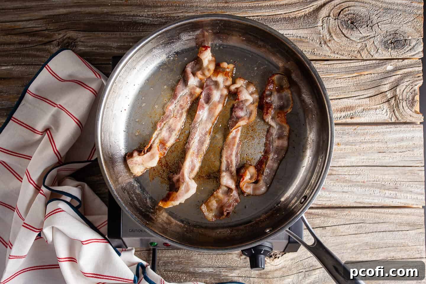 Rendering bacon in a large stainless steel skillet.