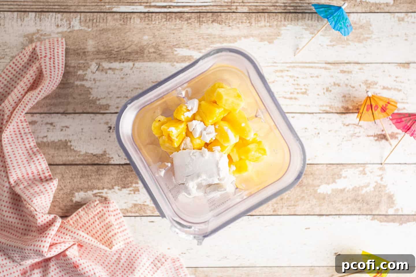 Frozen pineapple chunks, coconut milk, and rum in the pitcher of a blender.