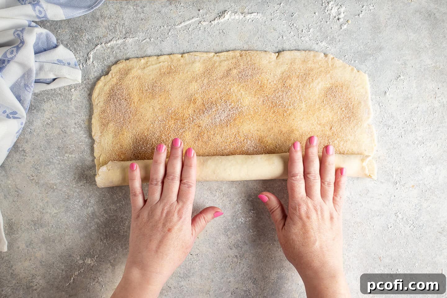 Croissant dough, sprinkled with cinnamon sugar, being rolled into a tight log.