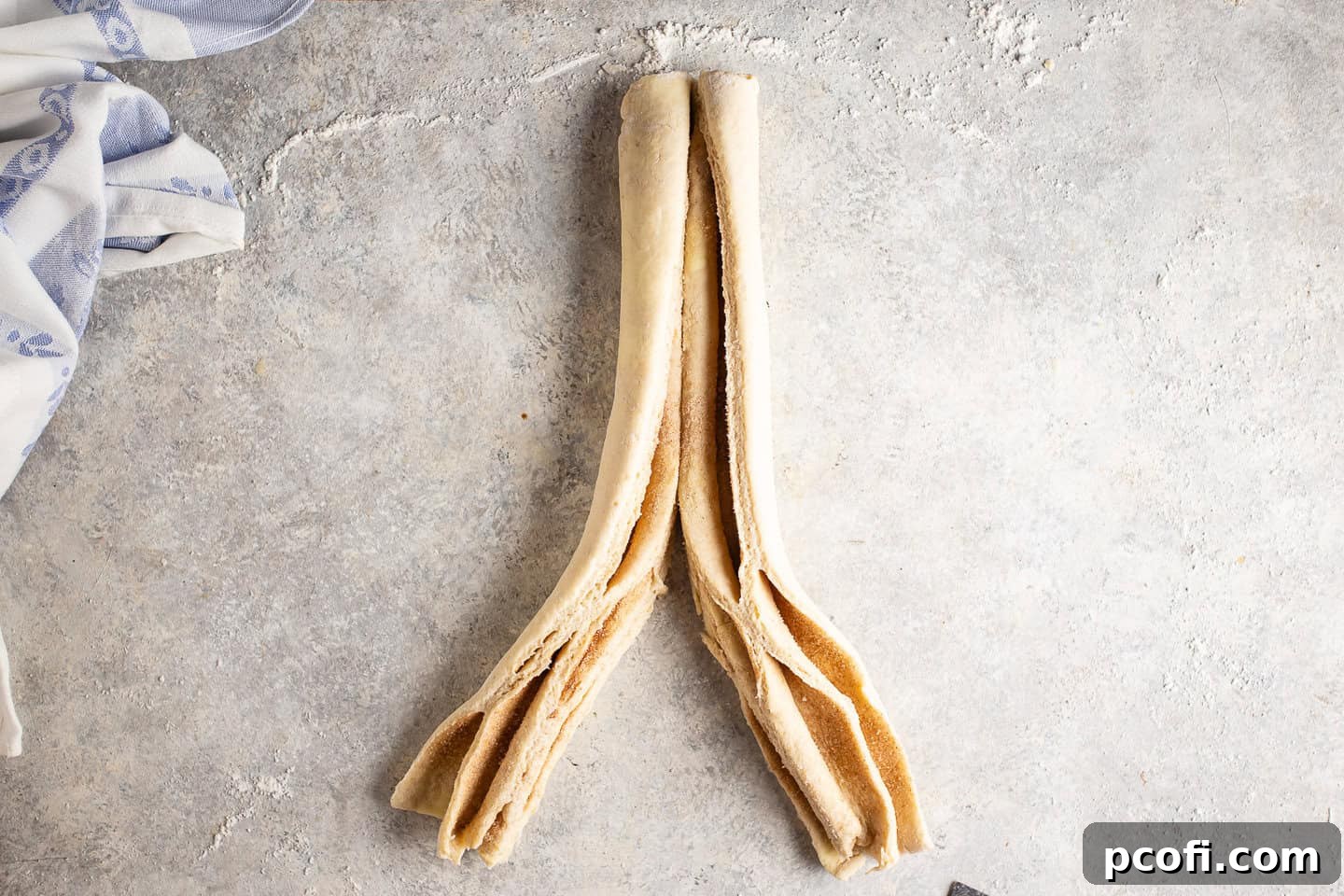 A cinnamon sugar-filled dough log being sliced in half lengthwise, revealing the layers.