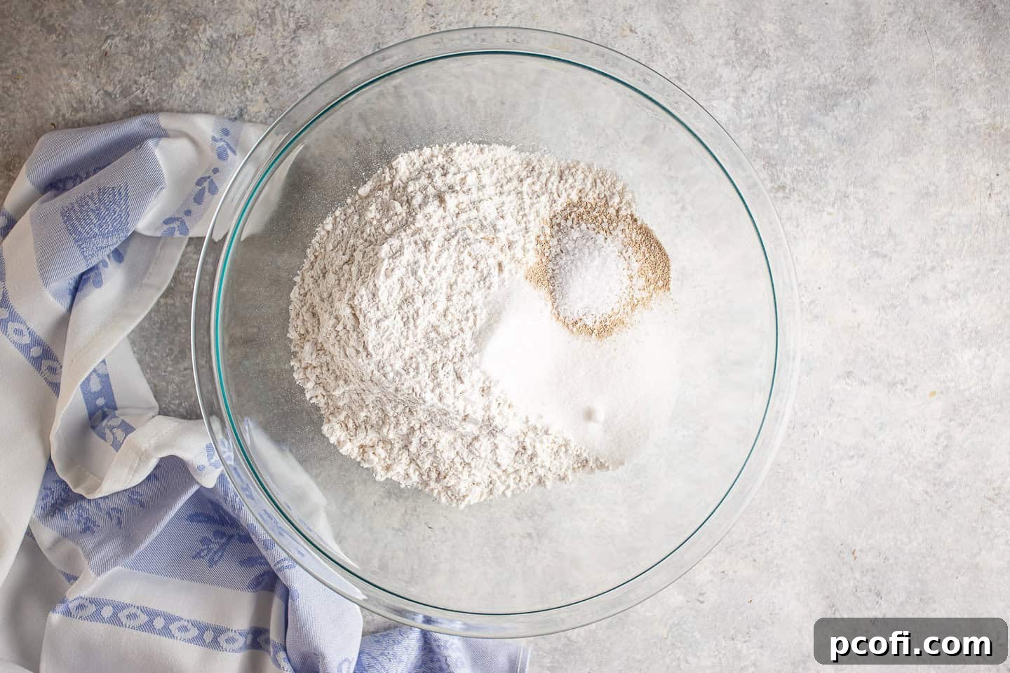 A large mixing bowl containing flour, sugar, yeast, and salt, ready for the next step.
