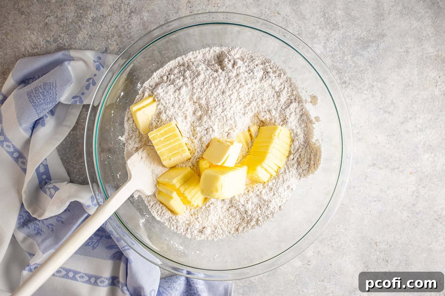 Cold butter slices being added to the dry ingredients in a mixing bowl.