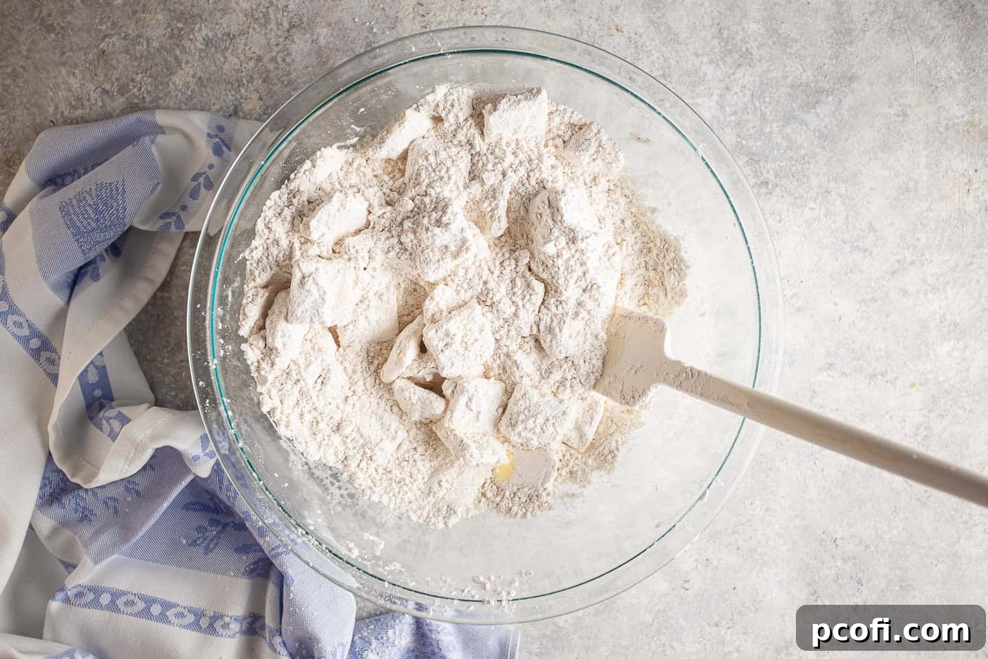 Butter slices, evenly coated in dry ingredients, scattered within the mixing bowl.