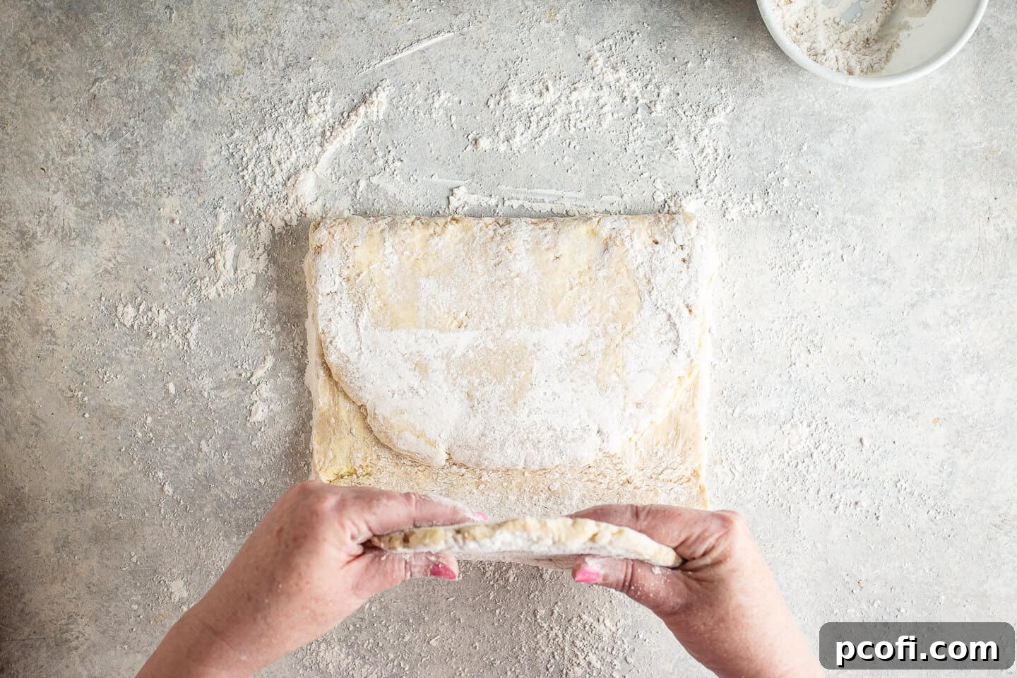 Croissant dough being folded into thirds, resembling a letter, during the lamination process.