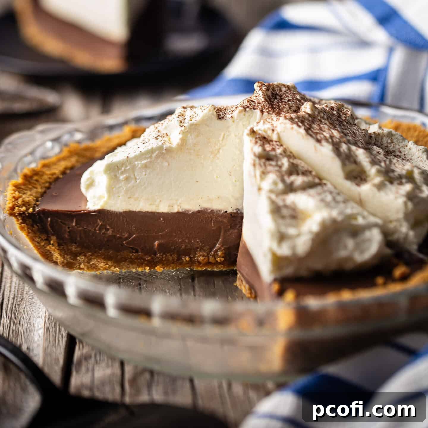 A stunning homemade chocolate pudding pie with a slice removed, revealing its rich, creamy chocolate filling and crunchy graham cracker crust, topped with generous swirls of whipped cream.