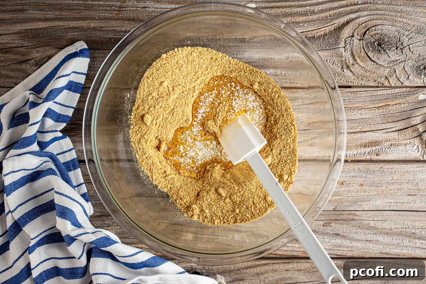Graham cracker crumbs and melted butter being mixed together in a large glass bowl, forming the base for the pie crust.
