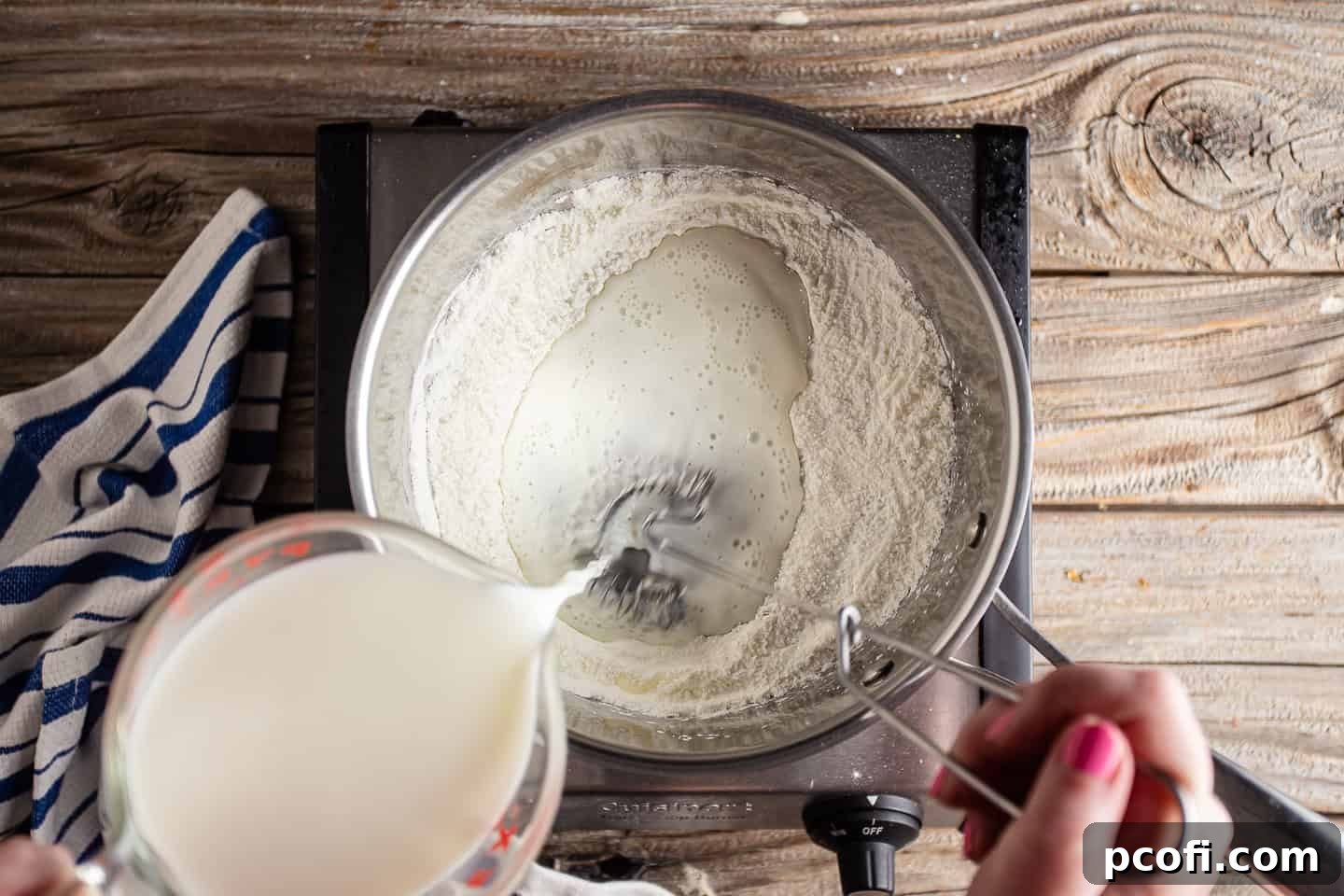 Milk is slowly whisked into the cornstarch and sugar mixture in a pot, ensuring a smooth, lump-free base for the pudding.