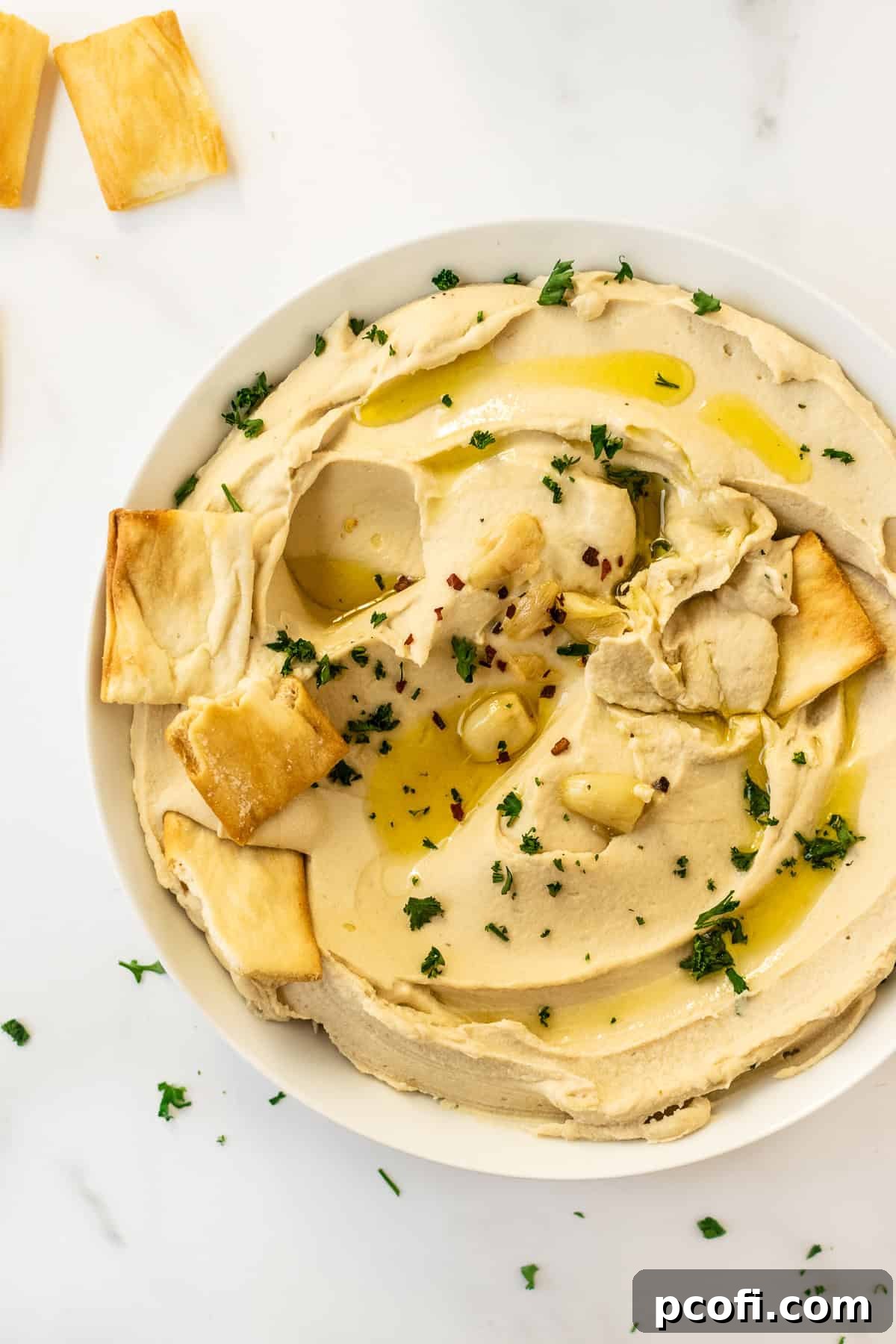 A bowl of creamy homemade hummus topped with fresh parsley, a drizzle of olive oil, and served with pita chips.