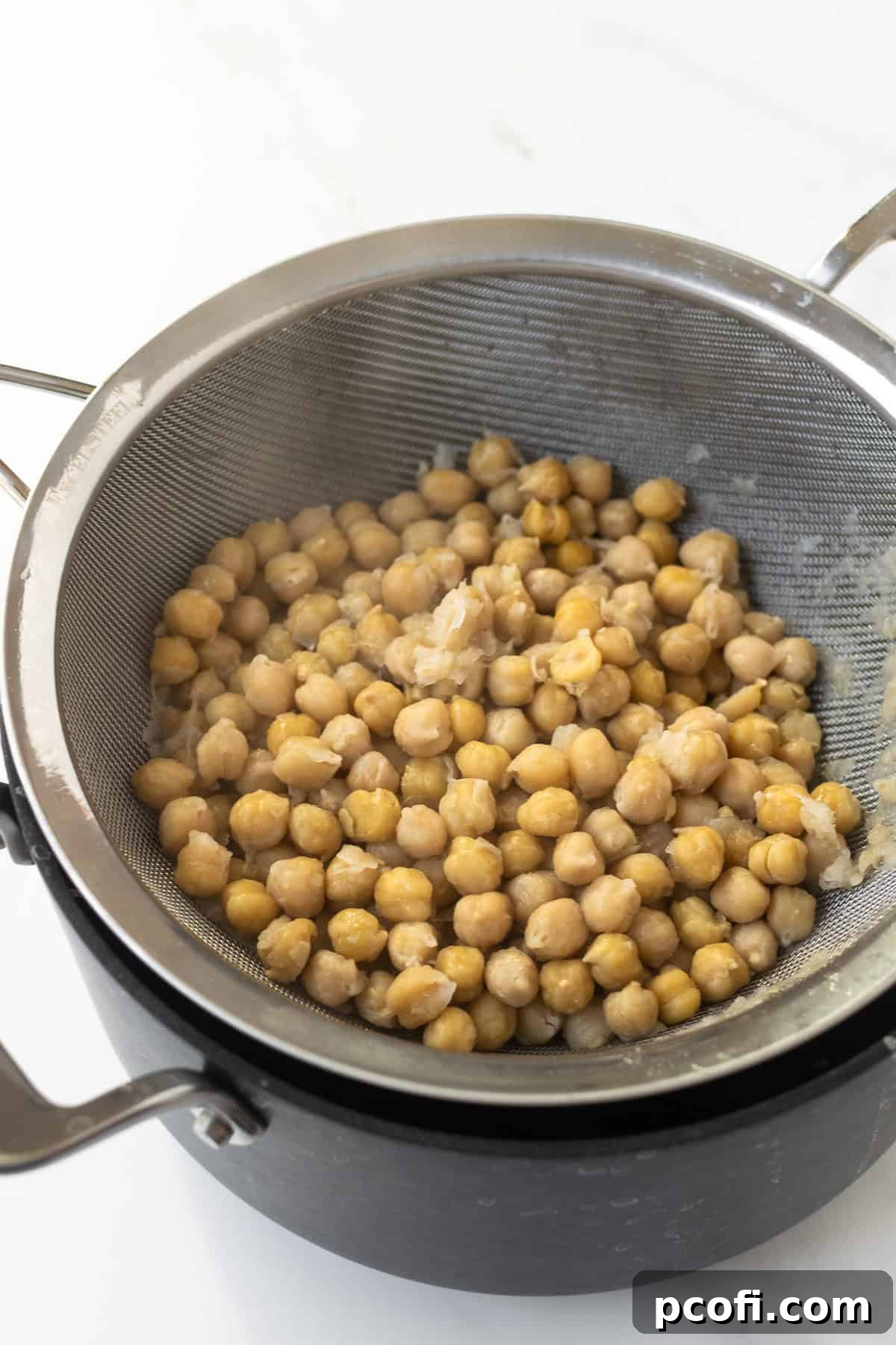 Boiled chickpeas in a strainer, resting in a black pot after being cooked with baking soda.