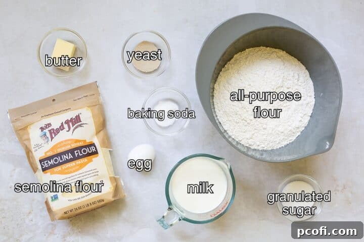A selection of raw ingredients for making English muffins, including flour, salt, sugar, yeast, milk, butter, and an egg.