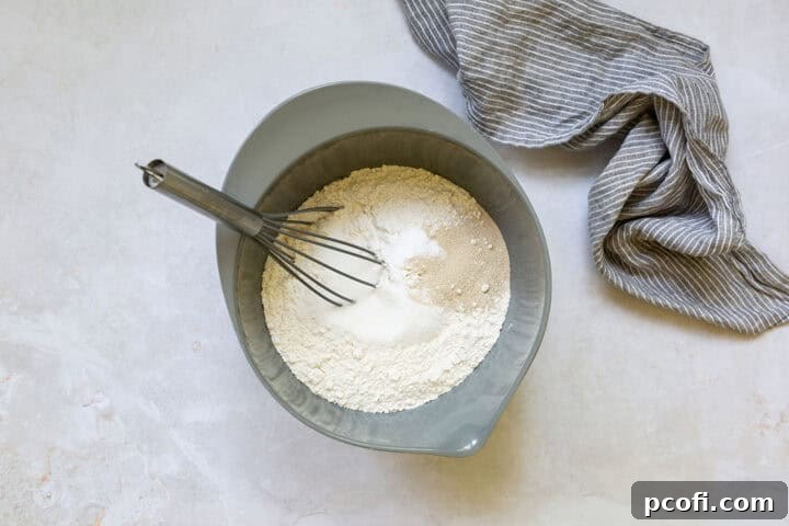 A bowl containing dry ingredients for English muffins: flour, salt, sugar, baking soda, and instant yeast.