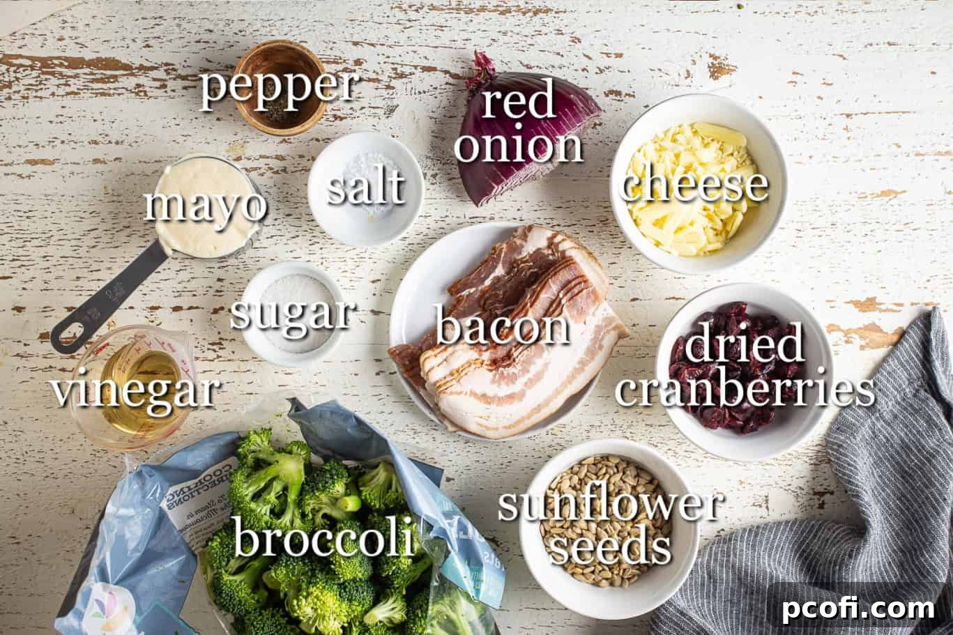 A curated selection of fresh ingredients for broccoli salad, neatly arranged on a rustic wooden board with informative text labels for easy identification.