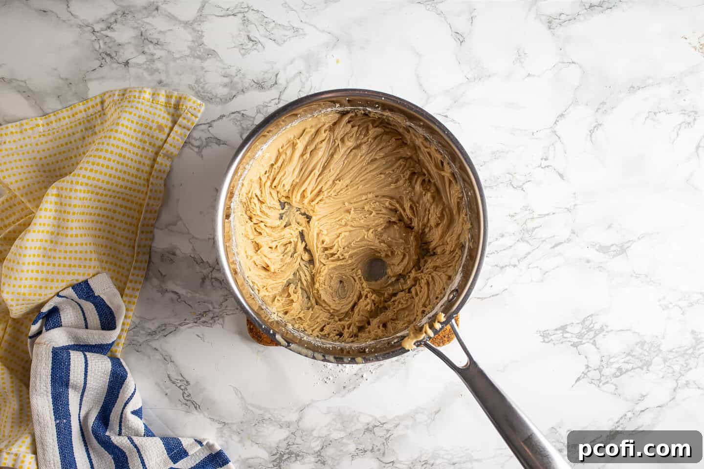 Butterscotch icing being beaten to a smooth, spreadable consistency with a hand mixer in the saucepan.