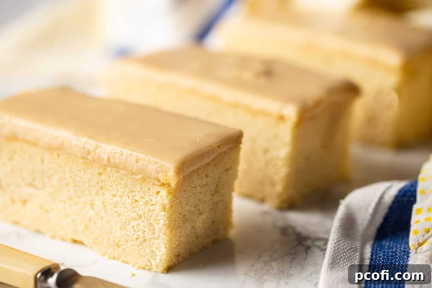 Individual butterscotch krimpets, freshly cut and neatly arranged, with a yellow and blue cloth adding a pop of color in the background.
