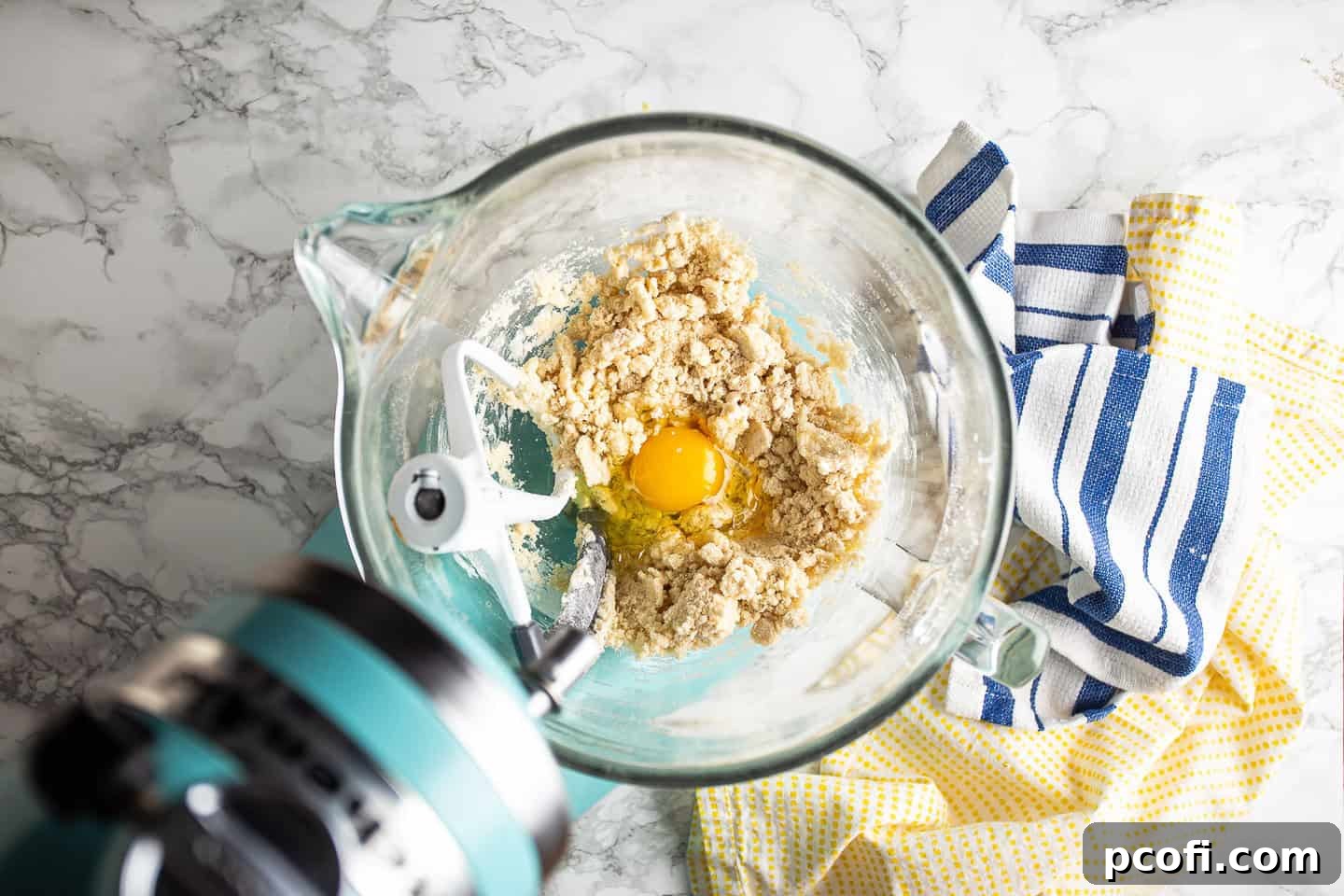 Cracking and adding eggs one by one into the butterscotch krimpet batter, ensuring full incorporation.