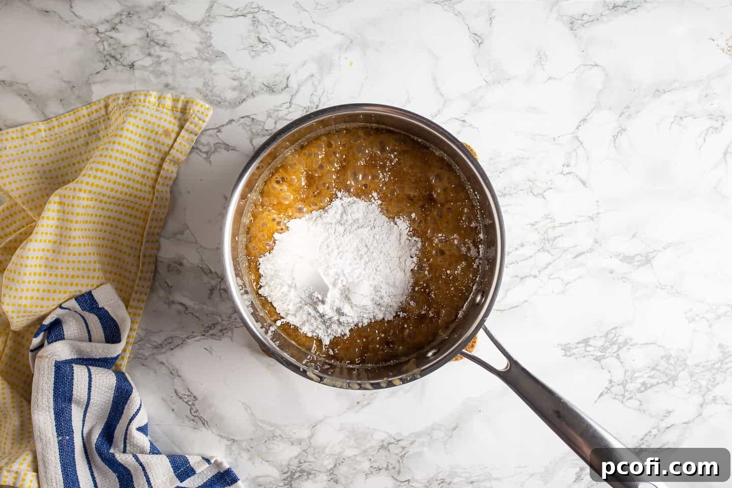 Adding the first half of powdered sugar to the hot butterscotch mixture in a pot, whisking vigorously.