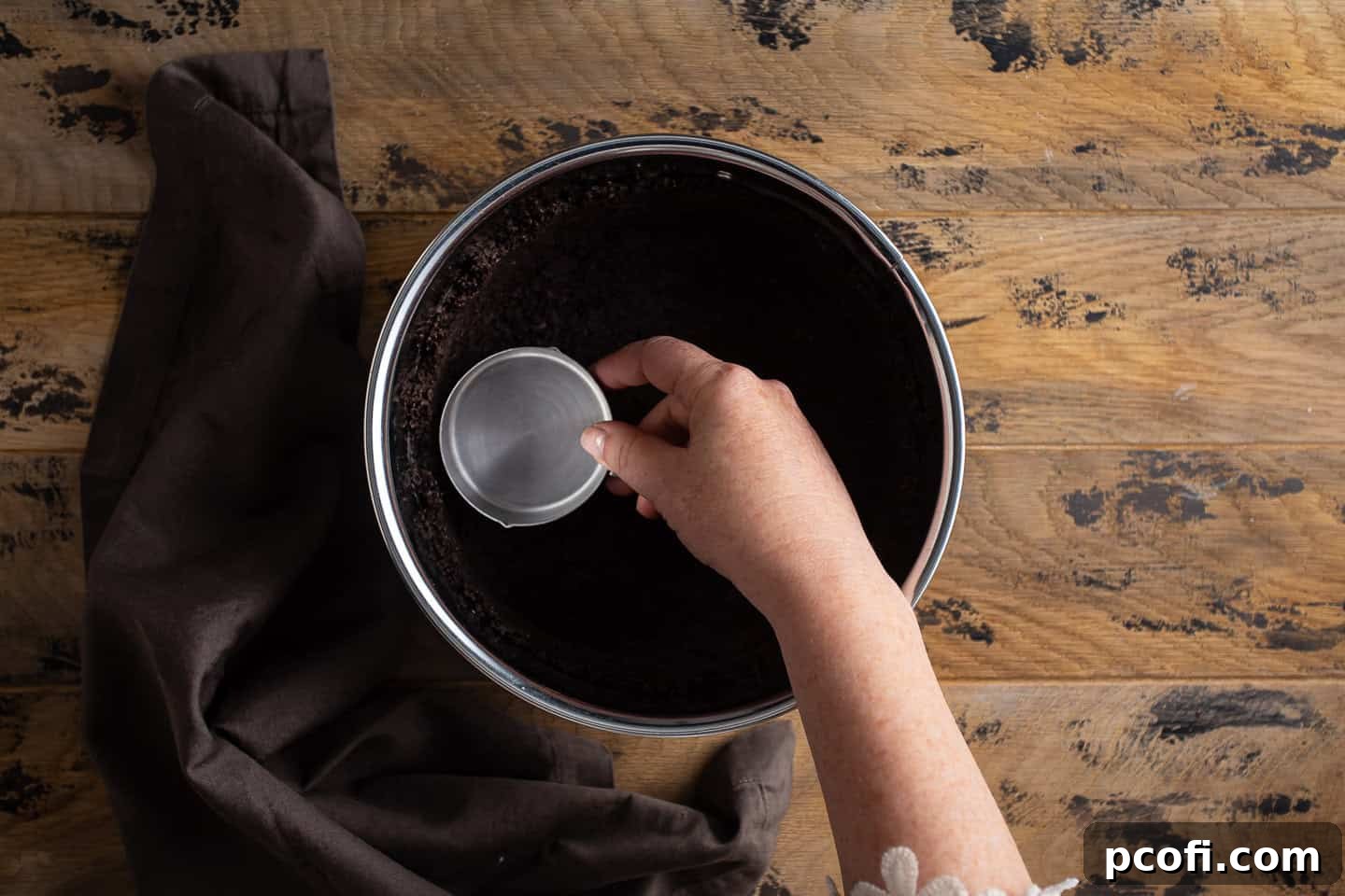 Pressing Oreo crust mixture into the bottom and up the sides of a springform pan using a measuring cup.