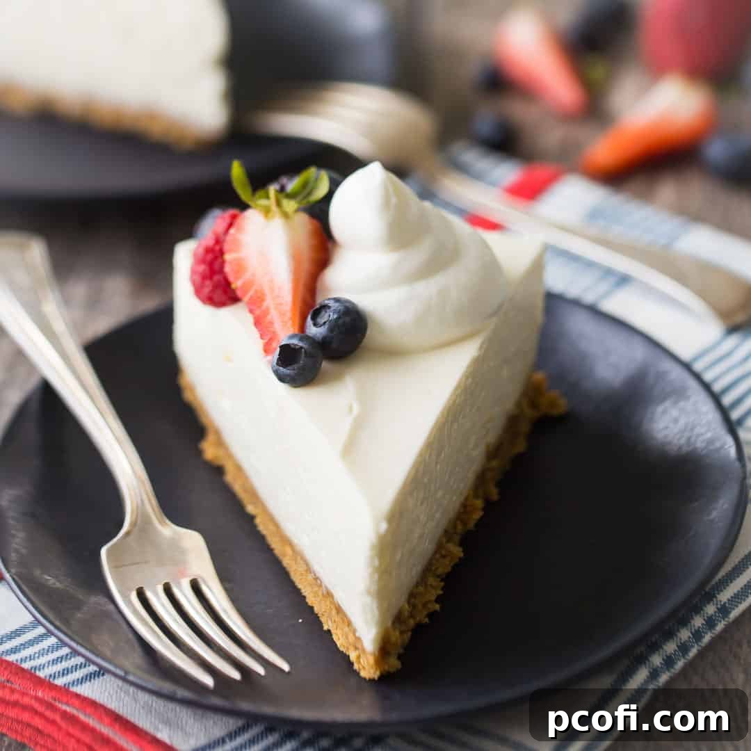 A perfect slice of no-bake cheesecake, garnished with light whipped cream and fresh berries, served on a dark blue plate with a vintage silver fork.