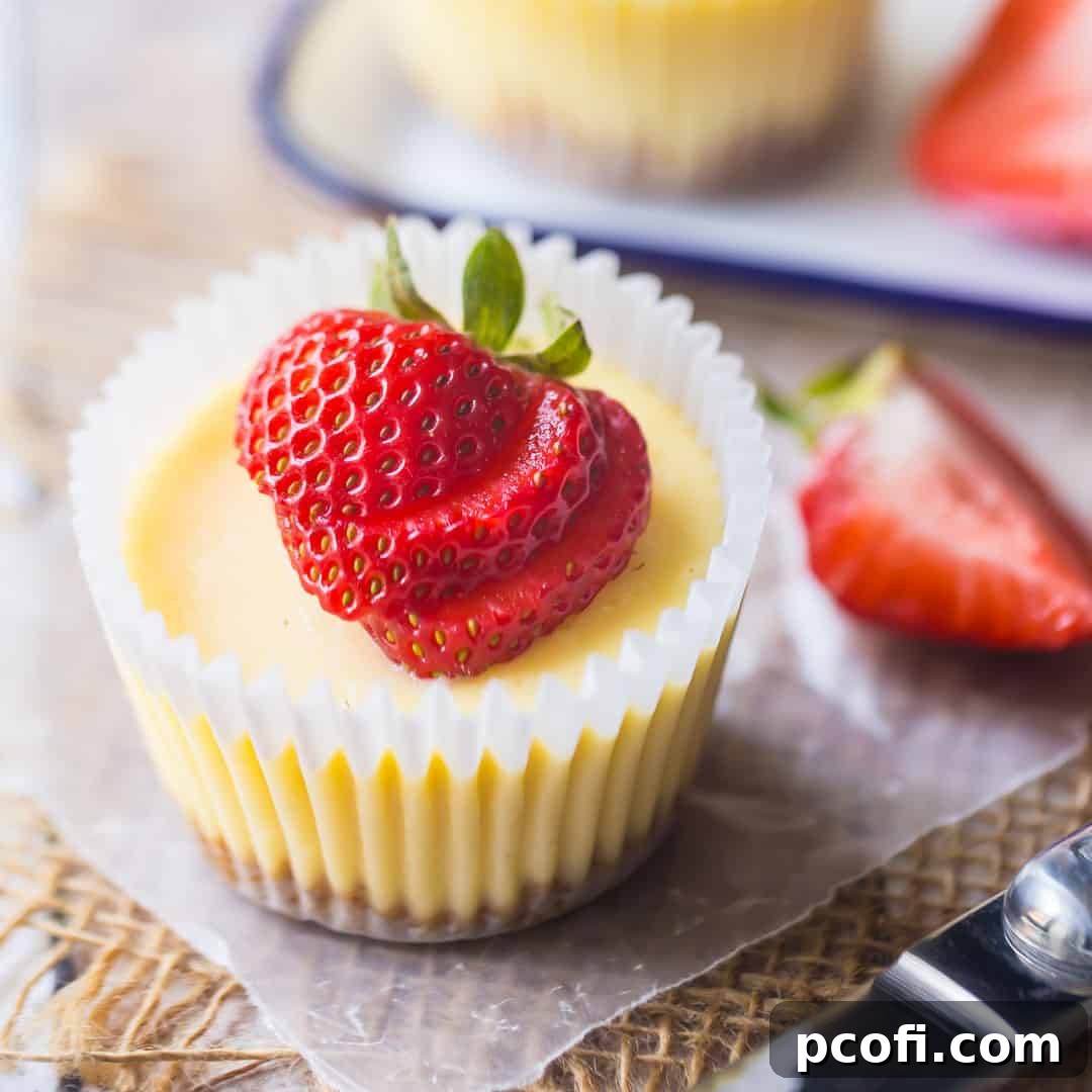 Charming individual mini cheesecakes, baked in a cupcake pan, with a graham cracker crust and a fresh strawberry garnish.