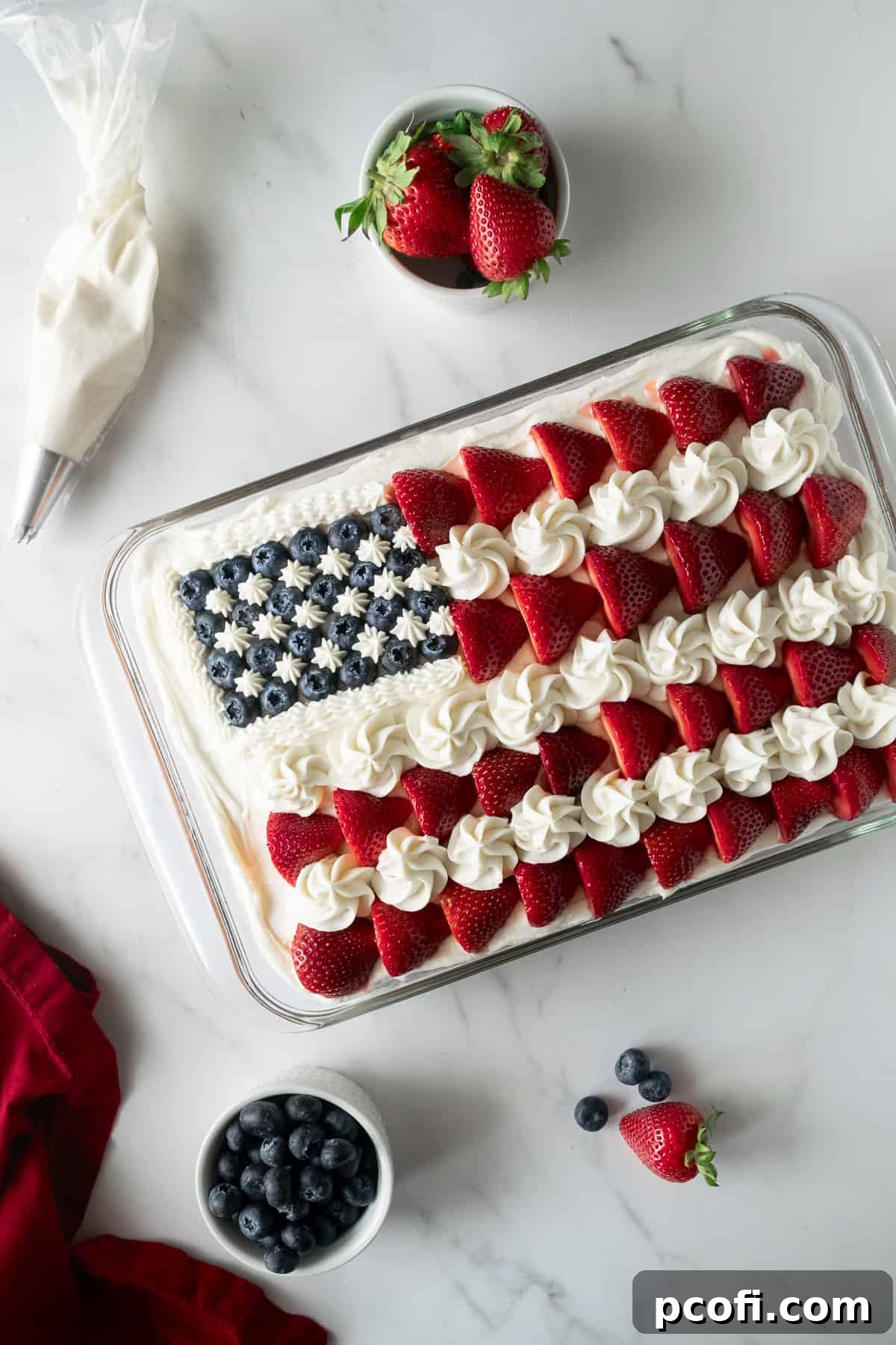 An impressive American flag cake in a baking pan, beautifully decorated with creamy vanilla frosting, fresh strawberries, and blueberries, ready for celebration.