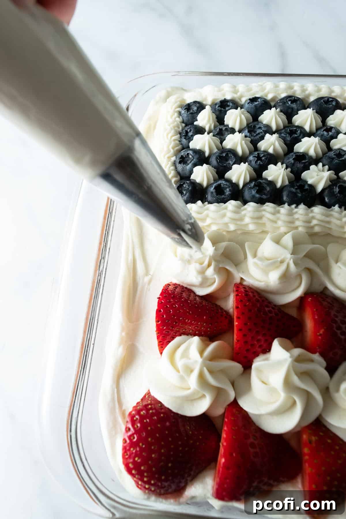 A close-up shot of piping white frosting stripes onto an American flag cake using a piping bag, demonstrating precision in decoration.