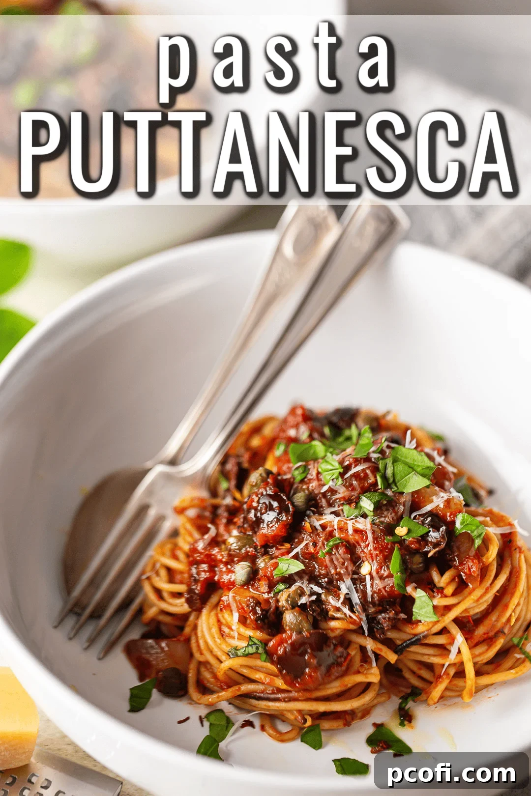 A serving of pasta puttanesca in a white bowl, garnished with freshly torn basil leaves. The vibrant red sauce, dotted with dark olives and capers, perfectly coats the spaghetti strands.