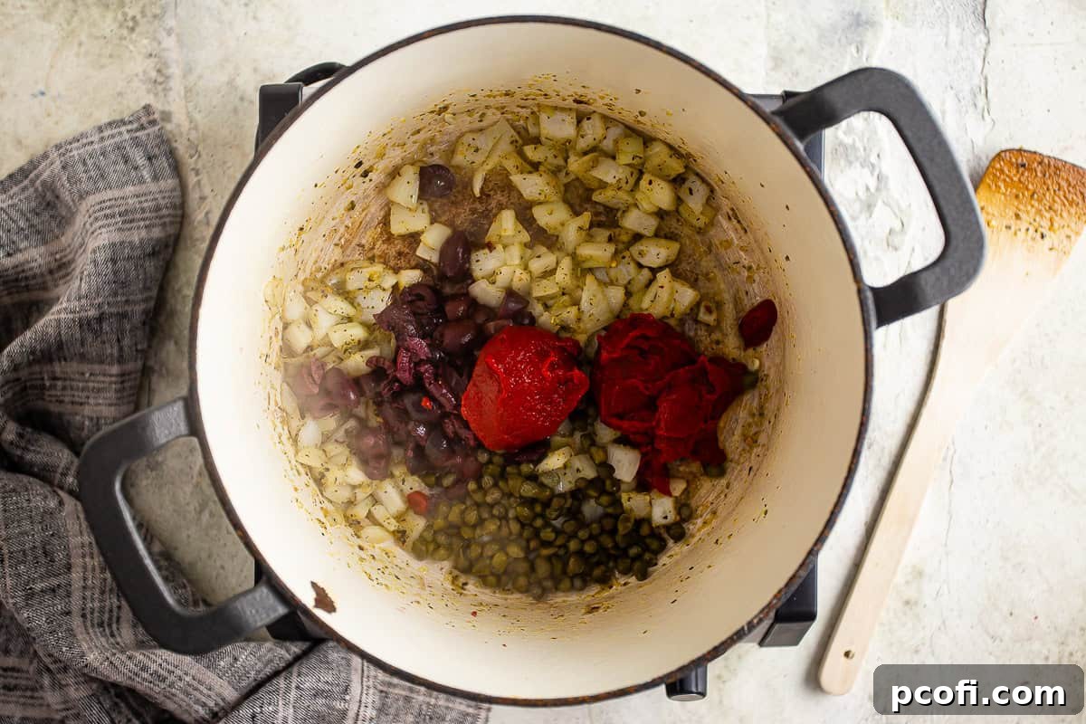 Adding chopped olives, capers, and rich tomato paste to the softened, seasoned onions in the pot, ready for the next stage of sauce development.