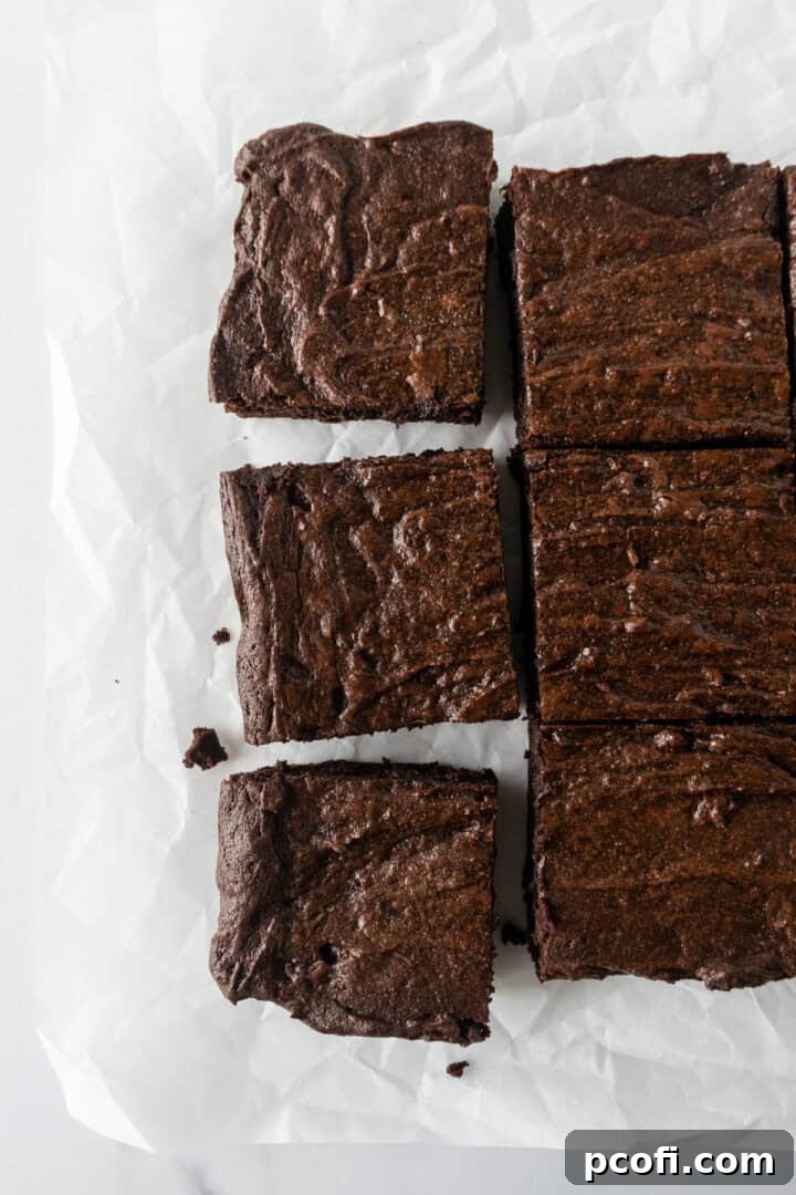 An inviting overhead shot of rich, fudgy brownies, perfectly cut into squares and arranged on parchment paper.