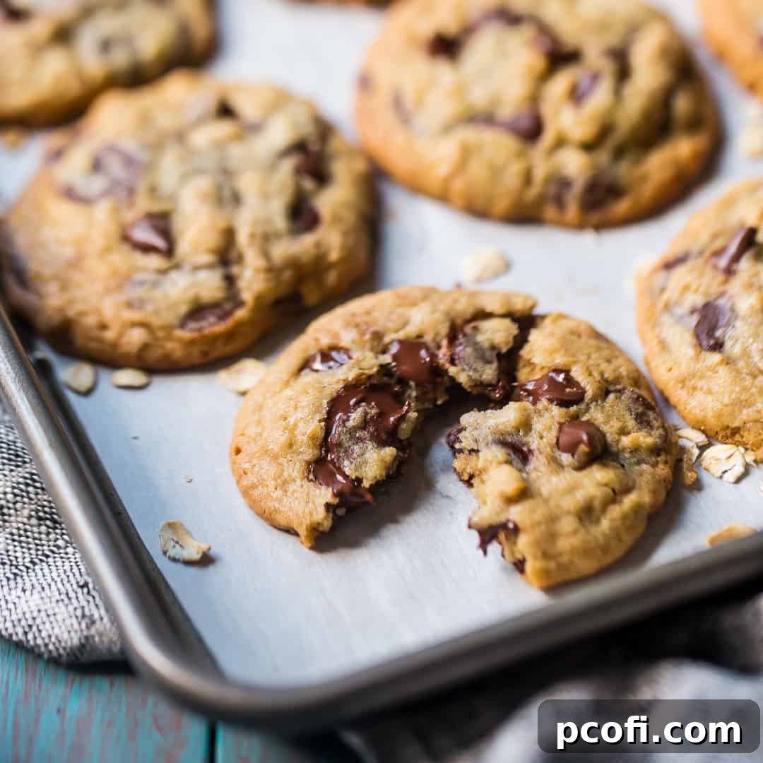 Close up image of a freshly baked oatmeal chocolate chip cookie, split in half to reveal pockets of melting dark chocolate.