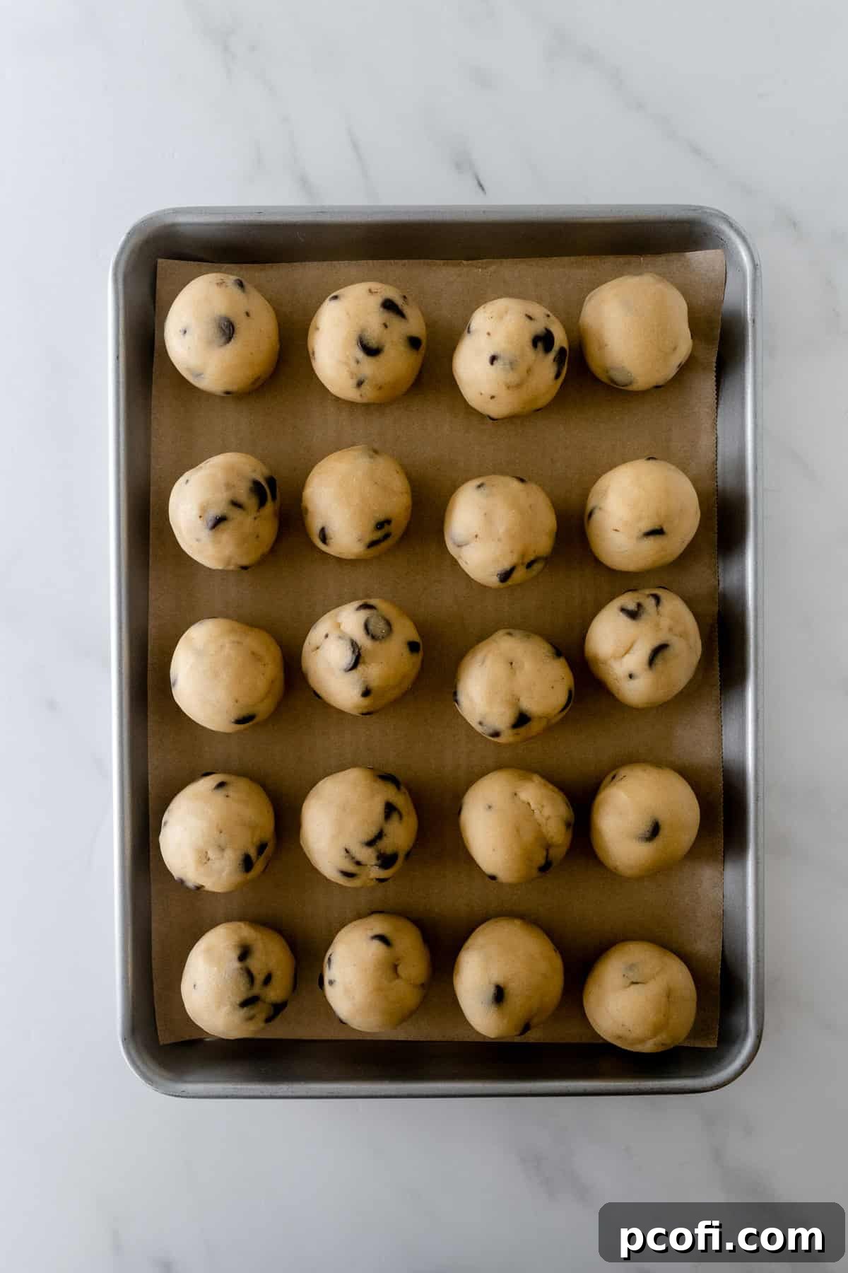 frozen cookie dough balls on a baking sheet lined with parchment paper, perfectly spaced and ready for transfer.