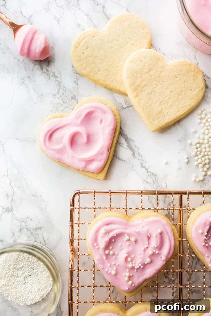 Vertical image of heart-shaped cream cheese cut-out sugar cookies on a copper cooling rack with delicate pink sugar cookie frosting.