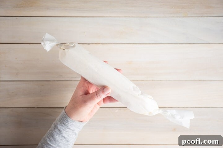 A log of butter cookie dough expertly wrapped in parchment paper, neatly tucked away, ready for chilling and future baking.