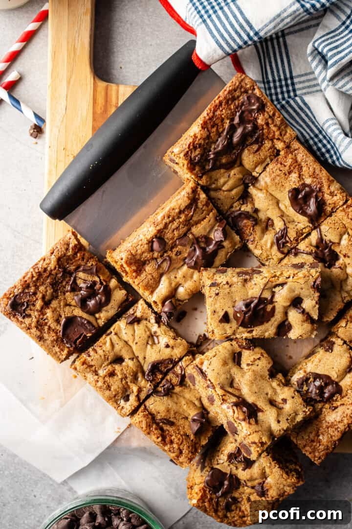 Cutting delicious chocolate chip blondie recipe into perfect squares with a pastry scraper on a cutting board.