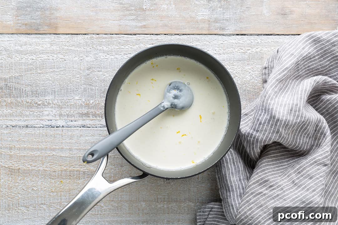 Heavy cream, sugar, and lemon zest simmering gently in a saucepan, the first step in making lemon posset.
