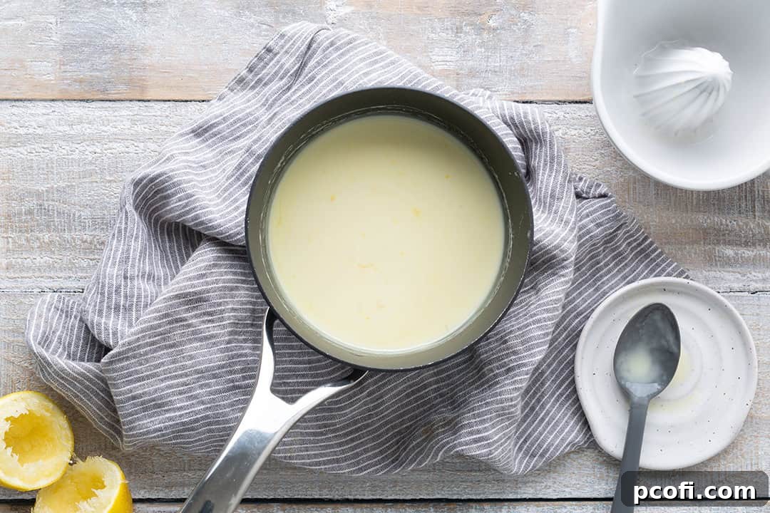 Fresh lemon juice being stirred into the hot cream mixture in a saucepan, beginning the thickening process.