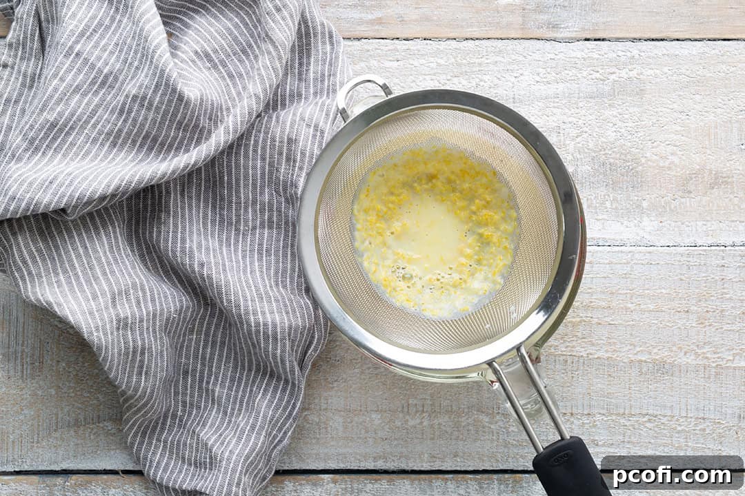 The lemon posset mixture being carefully strained through a fine-mesh sieve into a clean bowl.
