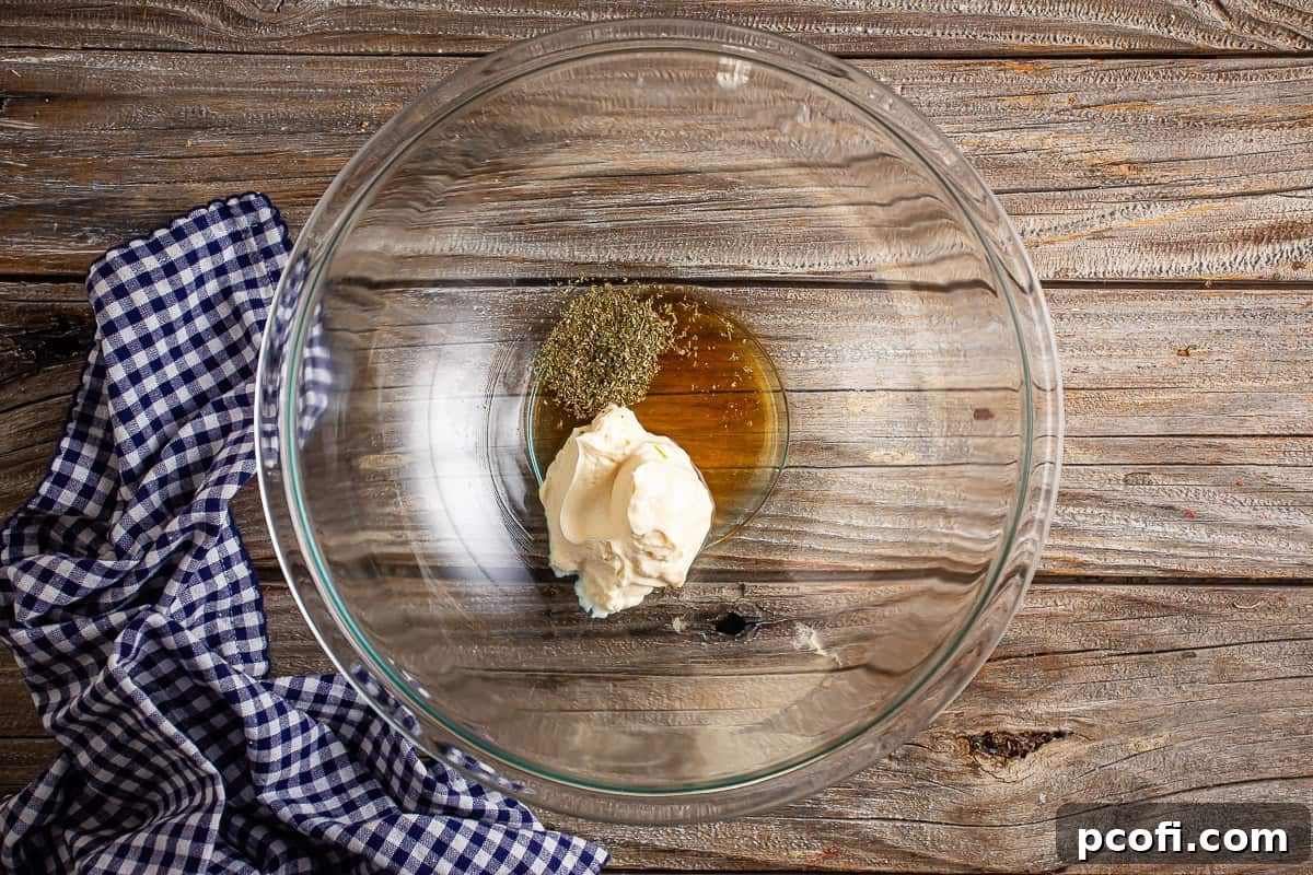 Mayonnaise, red wine vinegar, and Italian seasoning measured and placed in a large glass mixing bowl, ready to be whisked.