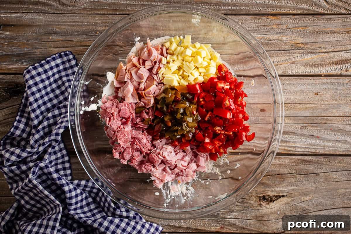 Chopped ham, salami, capicola, provolone, tomatoes, and peppers added to the glass bowl containing the dressing, ready for tossing.