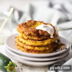 Crispy zucchini fritters stacked on a plate with a creamy sauce on top.