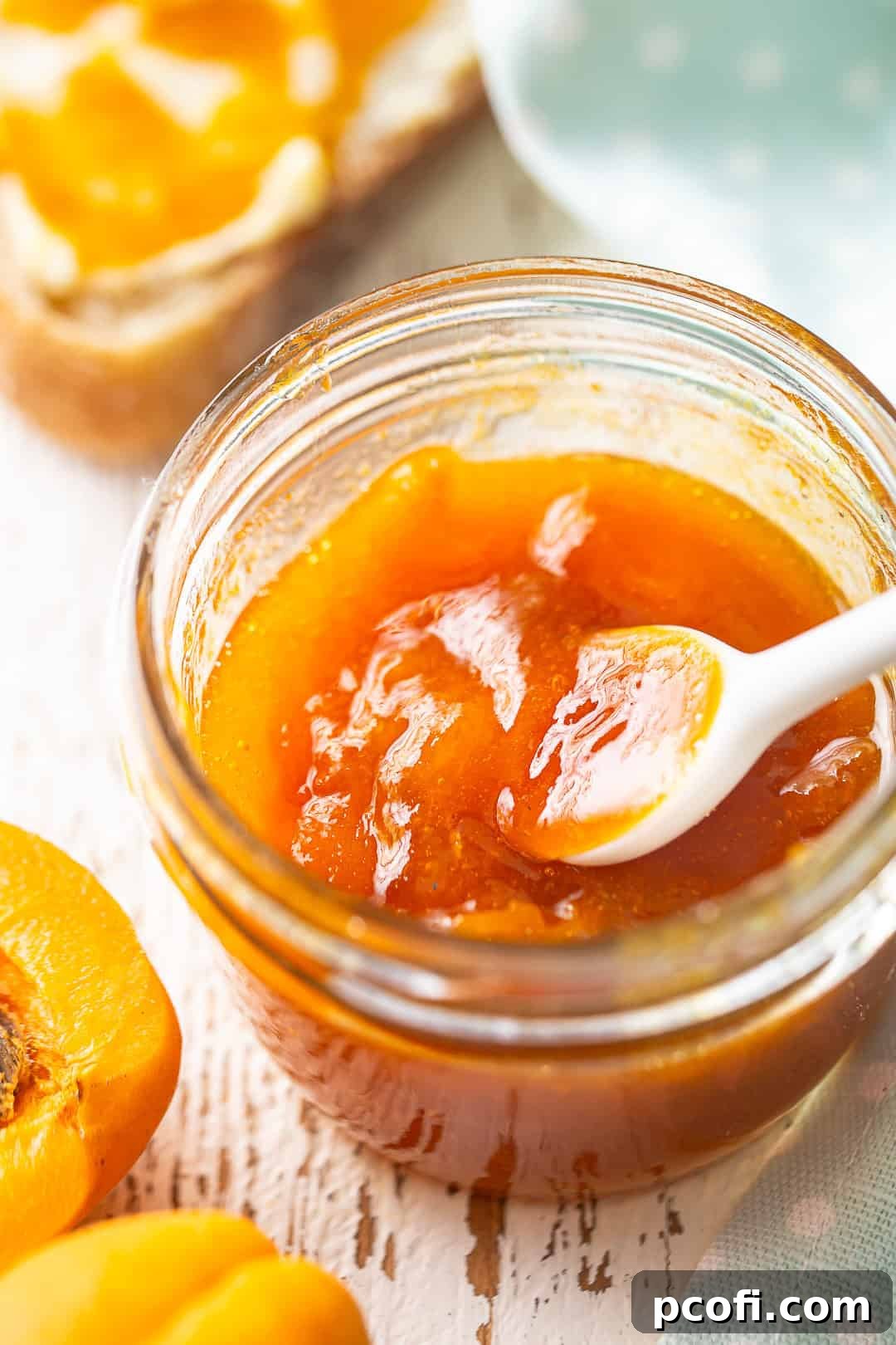 A close-up of a jar of apricot jam surrounded by fresh, ripe apricots on a rustic wooden surface.