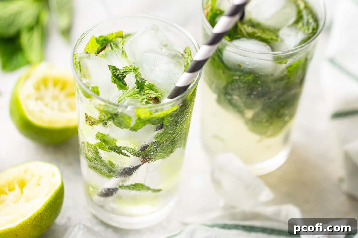 Mojitos elegantly presented in tall, clear glasses, each featuring black and white striped straws, alongside fresh lime and mint garnishes.